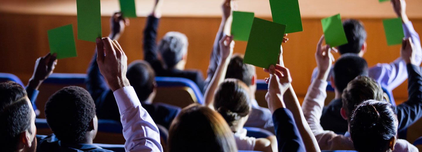 Menschen schauen auf Bühne und halten grüne Zettel in den Händen