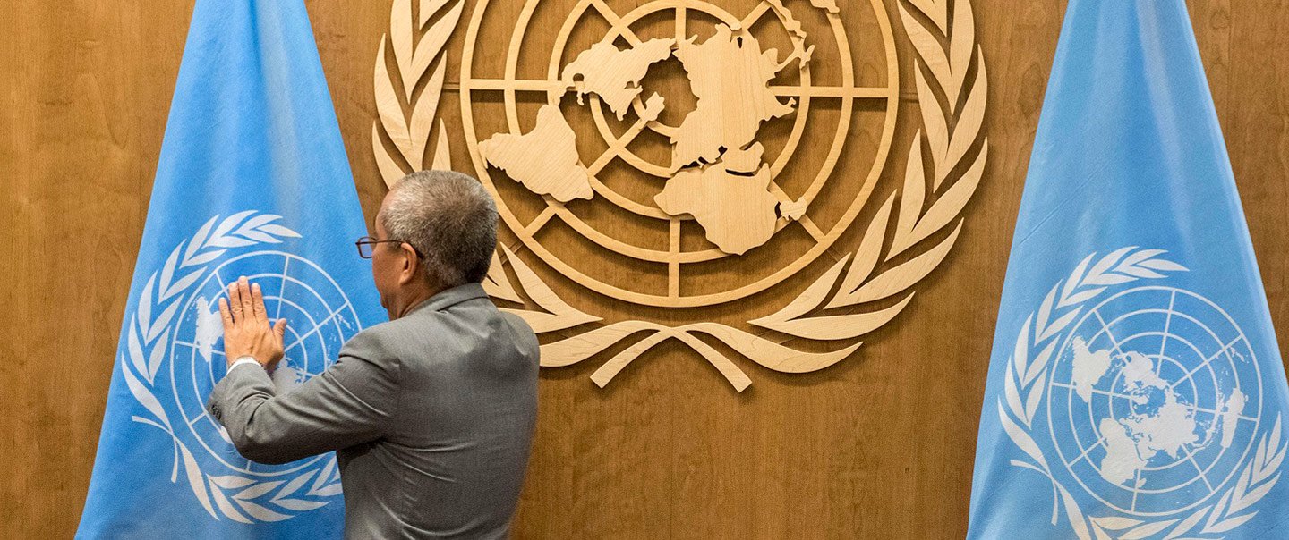 Ein Mann streicht eine aufgestellte Flagge der Vereinten Nationen glatt.