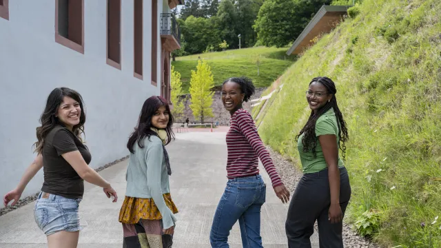 Das Bild zeigt Nacha, Garima, Diariou und Kiara, vier Schüler:innen des UWC Robert Bosch College in Freiburg, auf dem Schulhof. Sie lachen in die Kamera. 