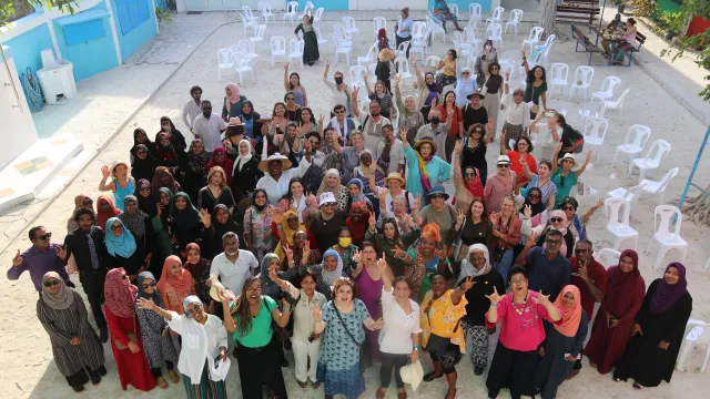 Eine große Gruppe von Frauen steht in einem Hof uns winkt in die Kamera. Das Bild zeigt Friedensstifterinnen auf einer Versammlung auf den Malediven 2025