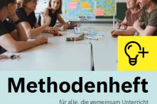 Menschen sitzen in einem Lehrerzimmer an einem Tisch, vor ihnen liegen Zettel und Stifte