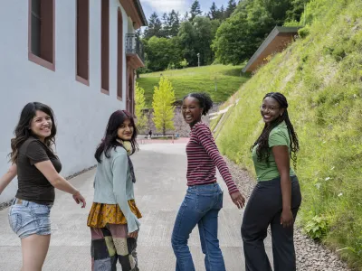 Das Bild zeigt Nacha, Garima, Diariou und Kiara, vier Schüler:innen des UWC Robert Bosch College in Freiburg, auf dem Schulhof. Sie lachen in die Kamera. 