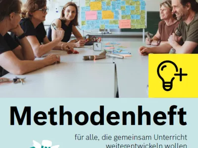 Menschen sitzen in einem Lehrerzimmer an einem Tisch, vor ihnen liegen Zettel und Stifte