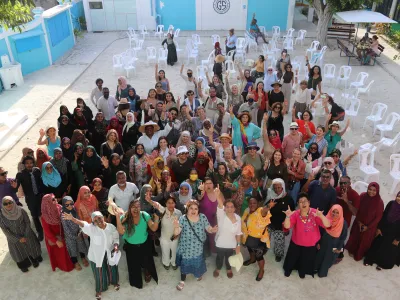 Eine große Gruppe von Frauen steht in einem Hof uns winkt in die Kamera. Das Bild zeigt Friedensstifterinnen auf einer Versammlung auf den Malediven 2025