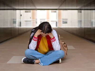 Upset school girl sitting on ground having problem with bullying
