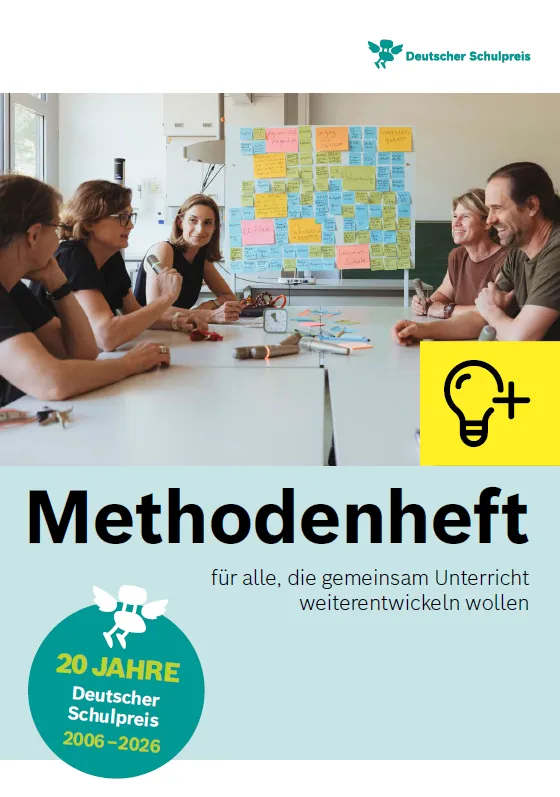 Menschen sitzen in einem Lehrerzimmer an einem Tisch, vor ihnen liegen Zettel und Stifte