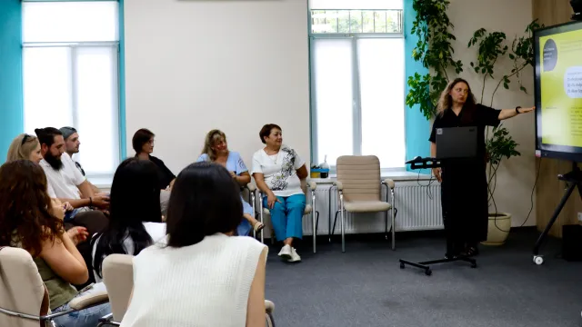 Menschen in einem Workshopt hören Alina Tokmylenko von der ukrainischen Organisation The Possible zu
