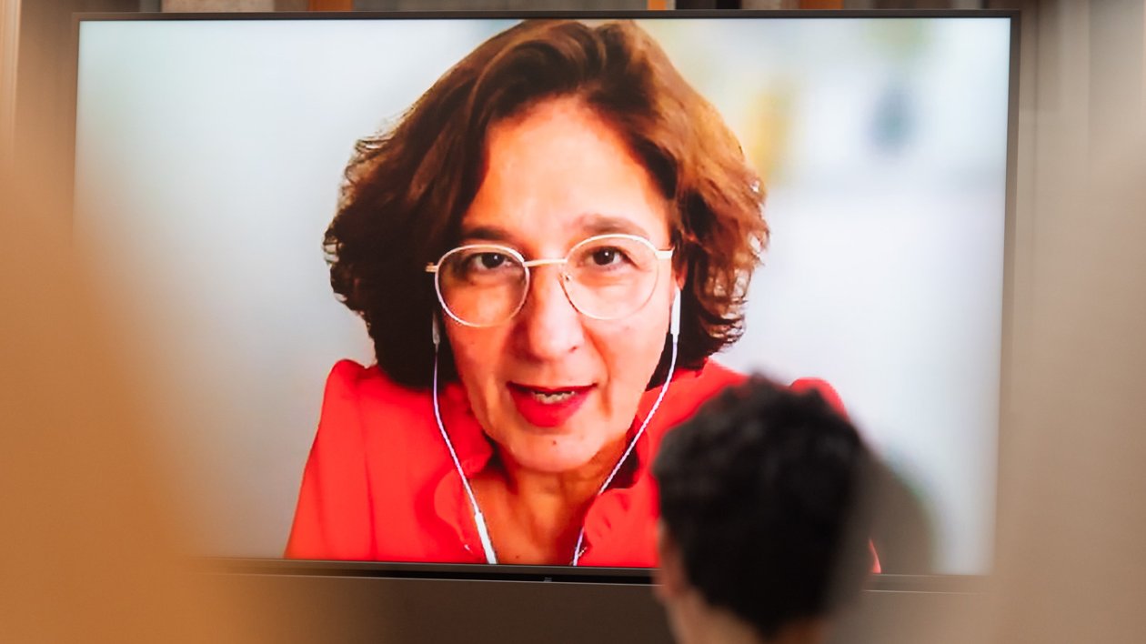 Die Journalistin Isabel Schayani ist bei einer Veranstaltung digital zugeschaltet und auf einer Leinwand zu sehen